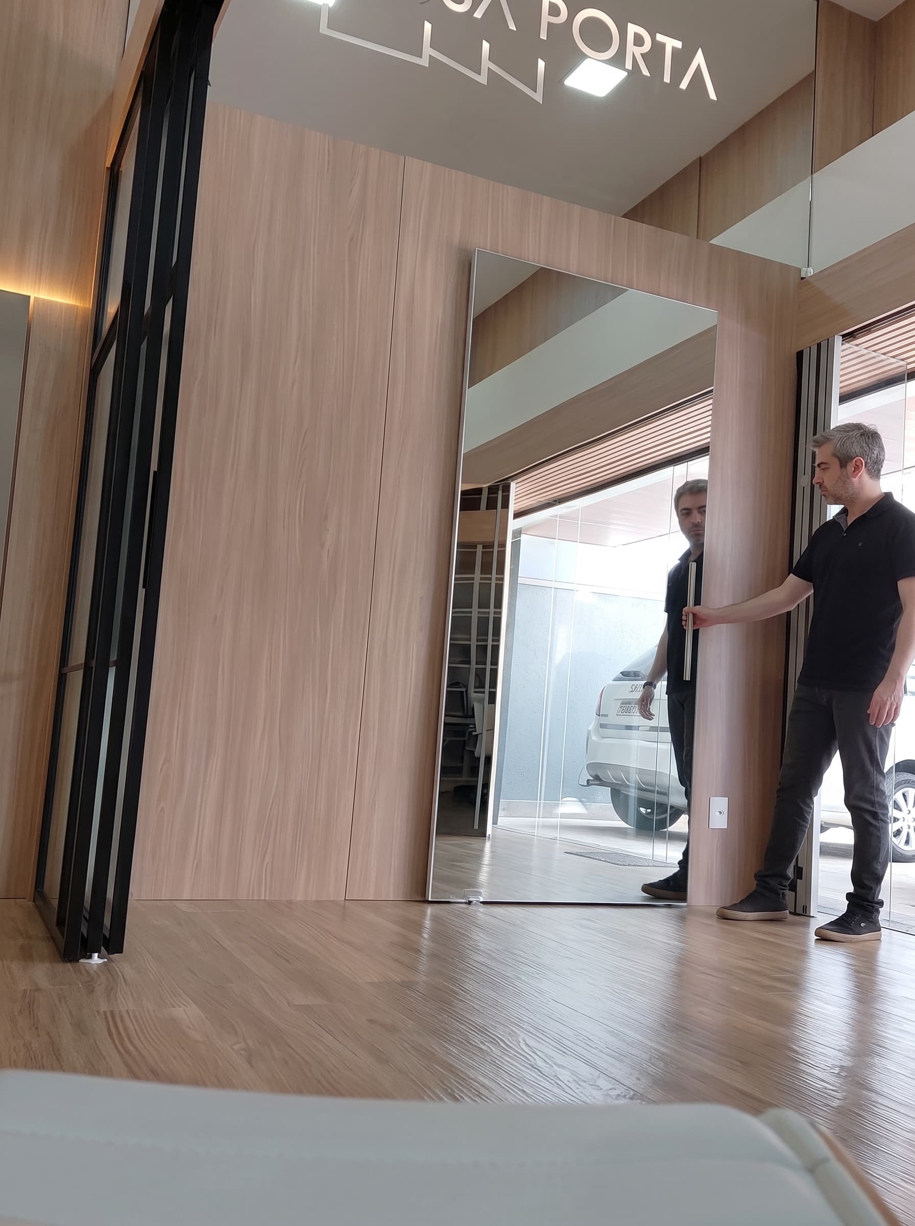 Entrada do showroom Nossa Porta — vidro espelhado que se camufla no painel de madeira, ferragem 100% oculta